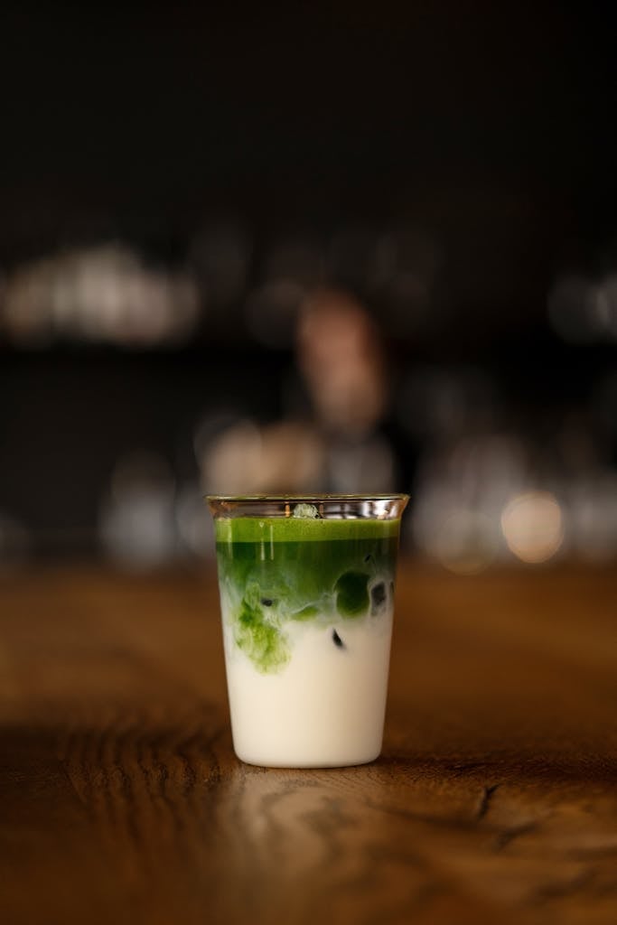 Elegant glass of matcha latte on wooden table, featuring layers of vibrant green matcha and creamy milk.