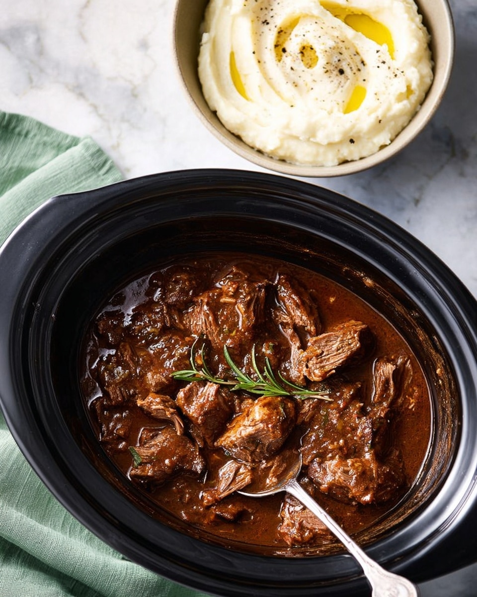 This image shows a black slow cooker filled with chunks of brown, tender-looking meat covered in rich dark brown sauce with a sprig of green herbs on top; a silver spoon rests inside the slow cooker. To the right, there is a white bowl containing creamy mashed potatoes with a swirl of olive oil and a sprinkle of black pepper on top. The background is a white marbled texture, and a green cloth is partially visible near the slow cooker. Photo taken with an iphone --ar 4:5 --v 7