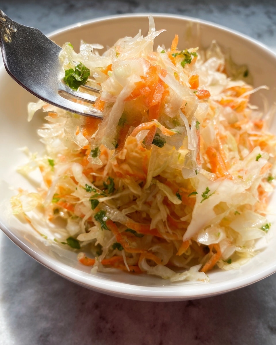 The image shows a close-up of a shredded salad served in a white bowl, placed on a white marbled surface. The salad consists of thin, translucent white cabbage shreds mixed with bright orange carrot strands and small green herb pieces scattered throughout. A metal fork holds up a small portion of the salad, highlighting the crisp and slightly moist texture of the vegetables. The lighting emphasizes the freshness and vivid colors of the salad. photo taken with an iphone --ar 4:5 --v 7