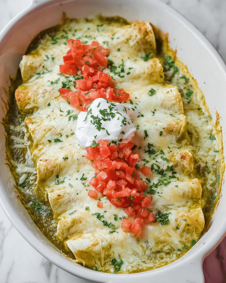 The dish shows five rolled enchiladas placed side by side in a white oval baking dish, covered in melted white cheese with a slight golden tint. Underneath the cheese, a green sauce is visible, filling the bottom of the dish and peeking through around the edges of the enchiladas. On top of the cheese, there are three small piles of bright red diced tomatoes spread evenly along the center. A dollop of white sour cream sits in the middle, sprinkled with finely chopped green herbs. Small scattered bits of green herbs are also spread across the entire surface of the melted cheese. The white baking dish sits on a white marbled surface. photo taken with an iphone --ar 4:5 --v 7