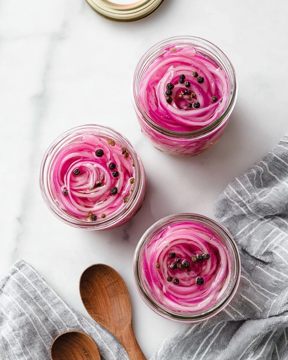 Three clear glass jars filled with thinly sliced pink pickled onions are placed on a white marbled surface, showing the onions tightly coiled in layers. Each jar has small black and green peppercorns sprinkled on top, resting in clear pickling liquid that gives a shiny texture to the onions. Two jar lids are placed open nearby, and a wooden spoon lies on the surface to the left. A grey and white striped cloth is folded on the right side, adding a soft contrast to the smooth marble beneath. Photo taken with an iphone --ar 4:5 --v 7