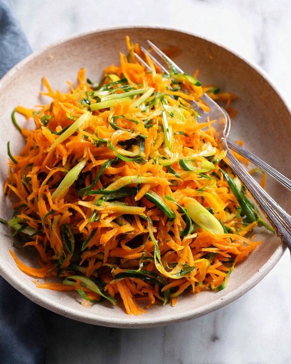 A bowl filled with shredded orange carrots mixed with thin slices of green vegetables, likely scallions, creating a vibrant contrast of colors. The carrots and greens make one visible layer, with a fresh and slightly moist texture. The bowl holding the salad is a natural light gray color, sitting on a white marbled surface, with two silver forks placed inside, one on each side of the pile of vegetables. The setting is simple and clean, focusing on the fresh colors of the food. Photo taken with an iphone --ar 4:5 --v 7