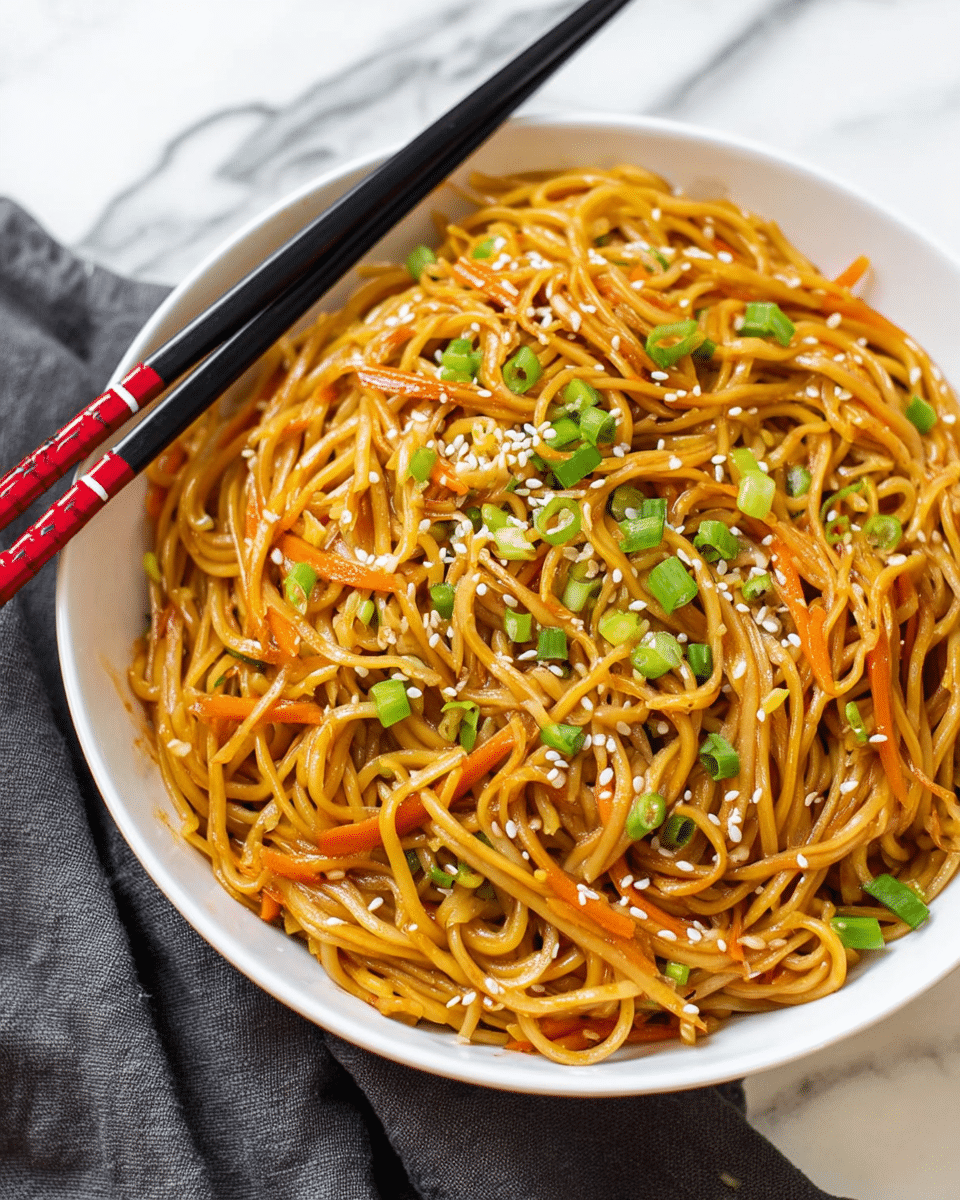 A white bowl filled with golden brown stir-fried noodles that are slightly glossy and mixed with small pieces of light orange carrot and translucent light brown onion slices. On top, there are scattered white sesame seeds and bright green chopped scallions, adding a fresh pop of color. Two chopsticks with black and red handles rest on the bowl’s edge. The bowl is placed on a white marbled surface with a dark gray cloth nearby. photo taken with an iphone --ar 4:5 --v 7