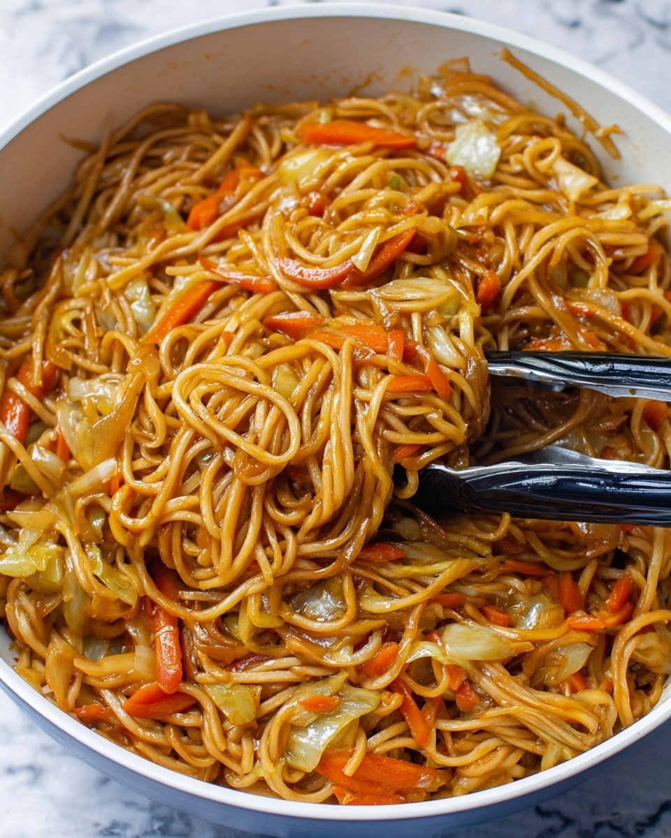 A large white bowl holds a serving of stir-fried noodles mixed with thinly sliced orange carrots and pieces of light yellow cabbage, all coated in a glossy brown sauce. The noodles are piled with some strands curling and overlapping, showing a soft and moist texture. Black and silver tongs lift a clump of noodles and vegetables from the center of the bowl. The background surface is a white marbled texture. photo taken with an iphone --ar 4:5 --v 7