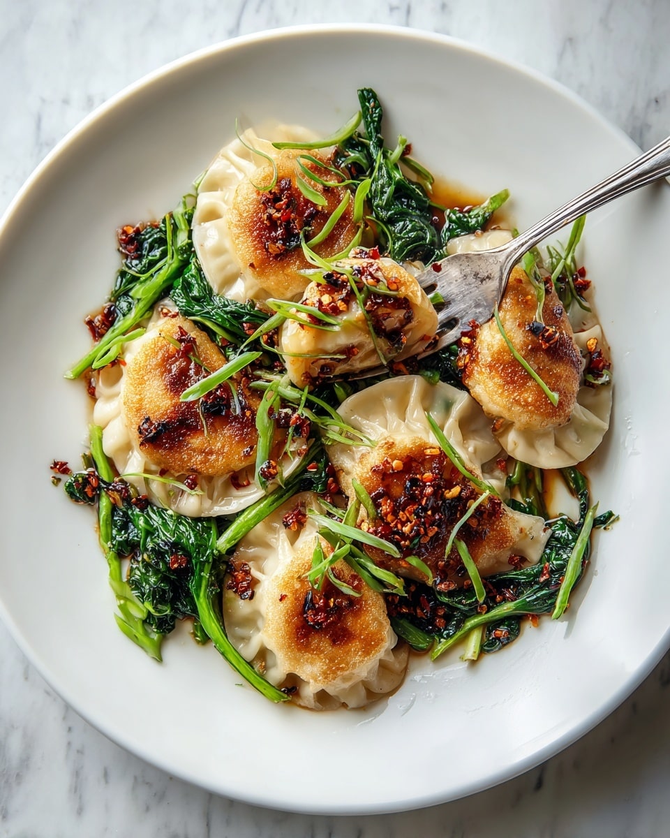 Five golden brown dumplings with ruffled edges are arranged in a loose circle on a white plate. They are topped with small bits of dark red chili oil and scattered green onion slices. Underneath the dumplings are bright green wilted leafy vegetables, adding a fresh contrast to the dish. A silver fork touches one dumpling from the top left side. The plate sits on a white marbled surface. photo taken with an iphone --ar 4:5 --v 7