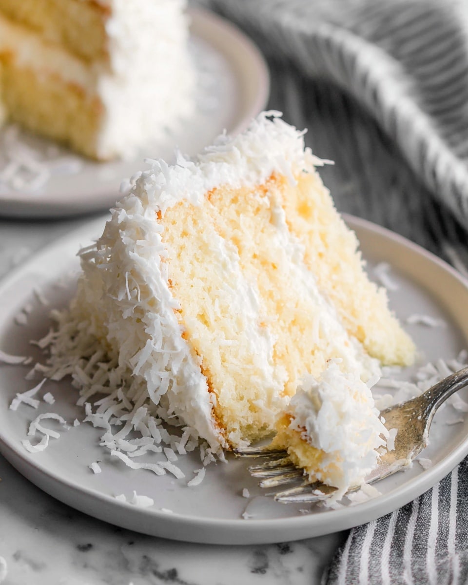 A slice of three-layer white cake rests on a white plate on a white marbled surface, with a silver fork partially cutting into the bottom layer. The cake has white fluffy frosting covering the top and sides, with shredded coconut sprinkled generously on the frosting and scattered on the plate. Inside, two layers of pale yellow custard or cream are sandwiched between the white cake layers, giving a moist, creamy look. The background shows another slice of cake out of focus and a striped cloth on the right side. Photo taken with an iphone --ar 4:5 --v 7