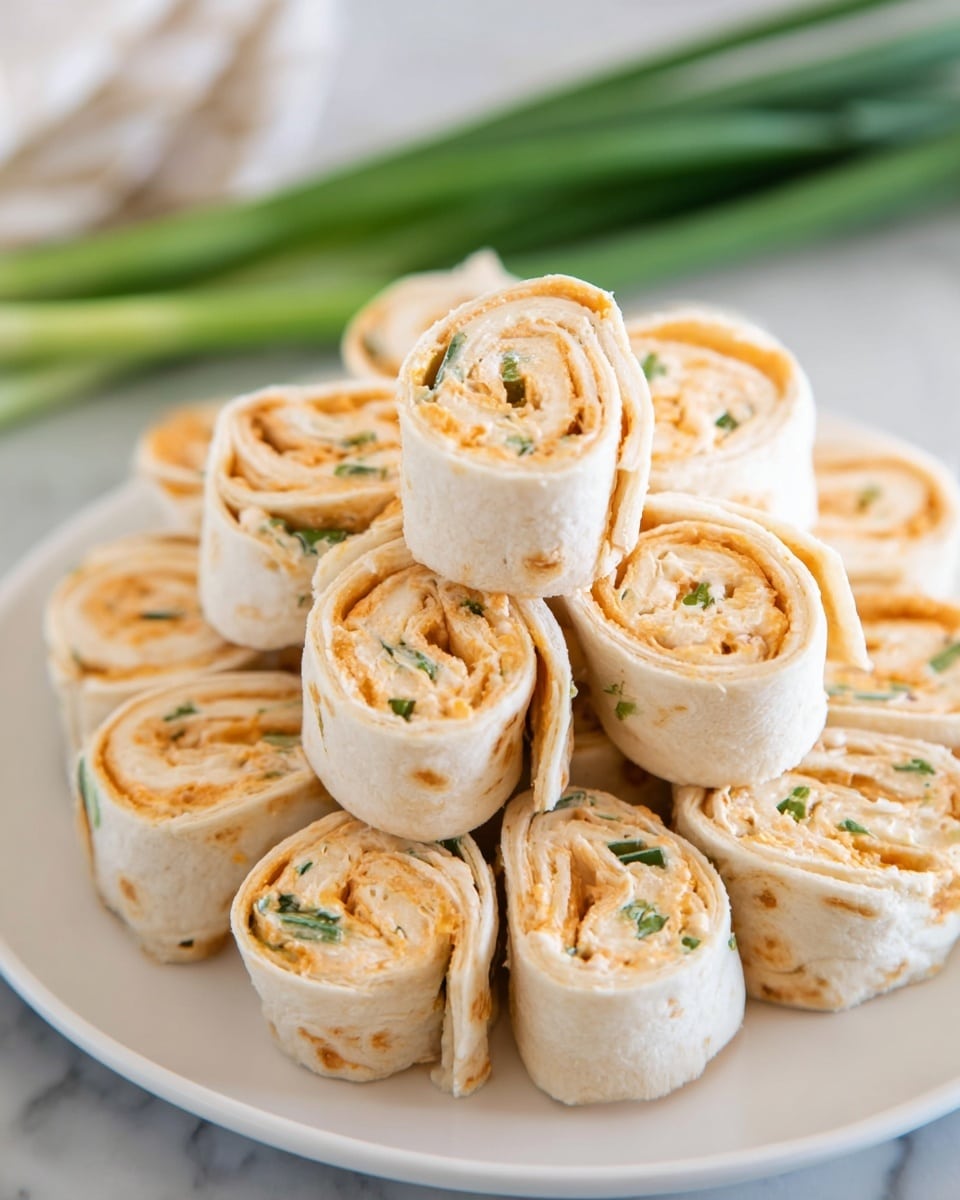 A white plate holds a tall pile of small tortilla roll-ups, each cut into thick slices showing swirled layers inside. The outer layer is a soft white tortilla, while the inside is filled with a creamy, light orange spread mixed with small green bits, likely herbs or chives. The roll-ups are neatly stacked on a white marbled surface background, with a blurred bunch of green onions in the back adding a fresh touch. photo taken with an iphone --ar 4:5 --v 7