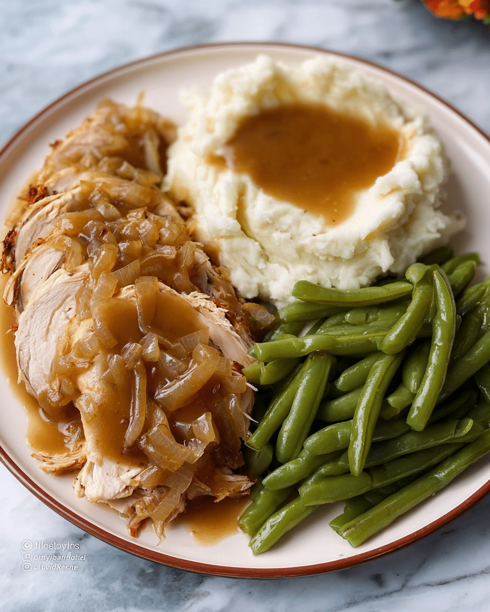 A white plate holds a meal with three main sections: on the left is sliced roasted turkey covered in shiny brown gravy with visible onion pieces, the slices stacked slightly overlapping; in the top center is a mound of smooth, creamy white mashed potatoes with a well in the middle filled with more brown gravy; on the right is a pile of green beans, cooked and glossy, arranged in a neat heap. The plate rests on a white marbled surface. Photo taken with an iphone --ar 4:5 --v 7