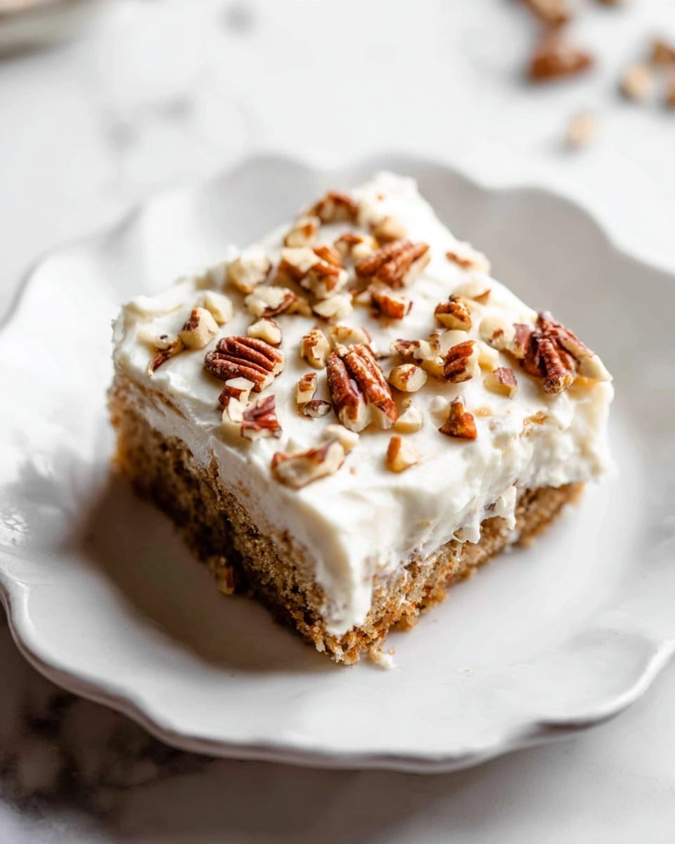 A square piece of cake sits on a white plate with a soft, wavy edge, placed on a white marbled surface. The cake has two visible layers: a light brown base layer with a moist texture and a creamy white frosting layer on top, which looks smooth and thick. The frosting is decorated with uneven pieces of chopped brown pecans scattered over the surface. The overall look is simple and inviting, with a homemade feel. photo taken with an iphone --ar 4:5 --v 7