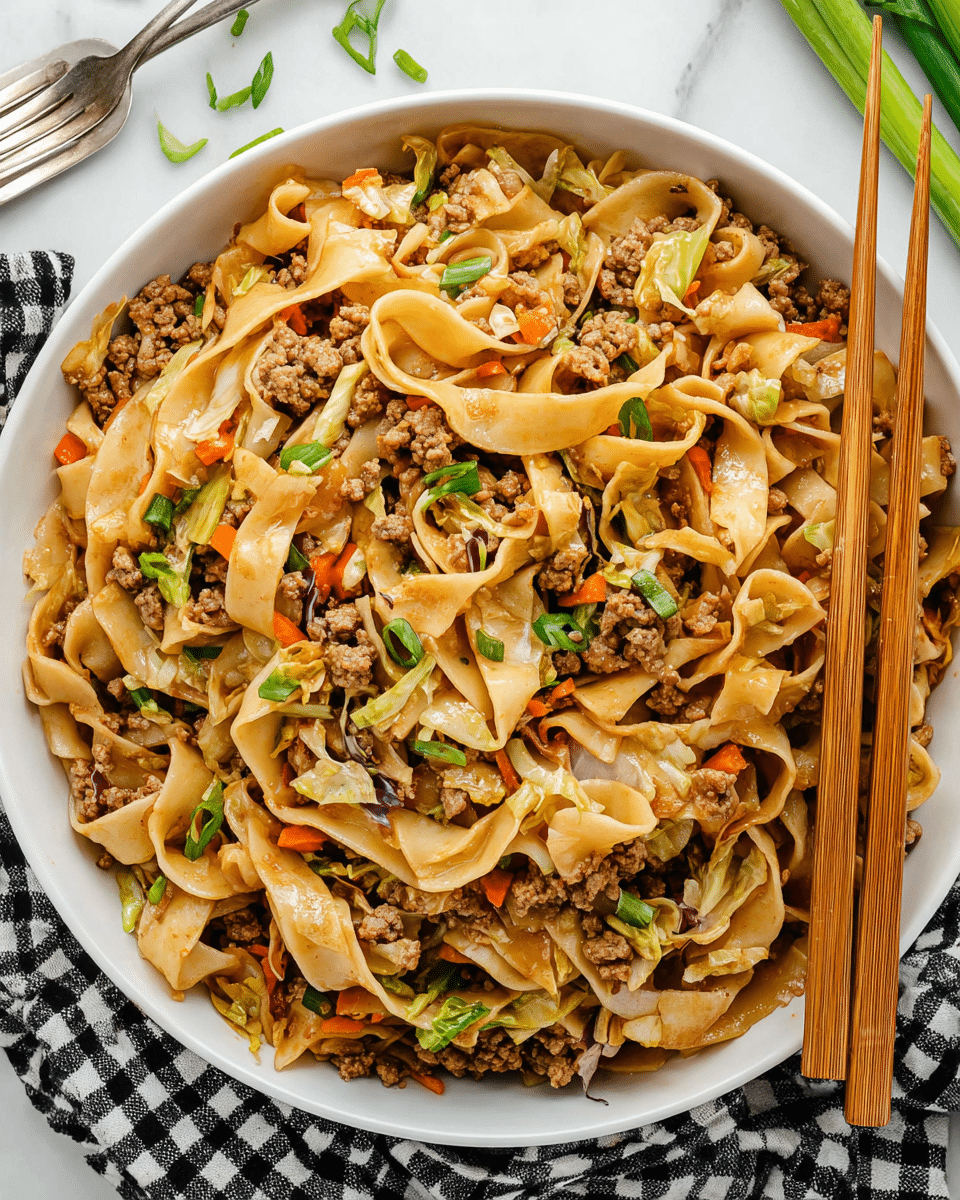 A close-up top view of a large white bowl filled with stir-fried wide noodles mixed with ground meat, small carrot pieces, chopped cabbage, and green onion slices. The noodles are light brown with a glossy texture, twisted and layered thickly inside the bowl. The ground meat is evenly scattered throughout, cooked to a golden brown color. Bits of orange carrot and white cabbage mix with the noodles and meat, with small bright green onion pieces sprinkled on top. A pair of wooden chopsticks rests on the right edge of the bowl. The bowl sits on a black and white checkered cloth placed on a white marbled surface, with a silver fork nearby and some green onion parts scattered around. Photo taken with an iphone --ar 4:5 --v 7