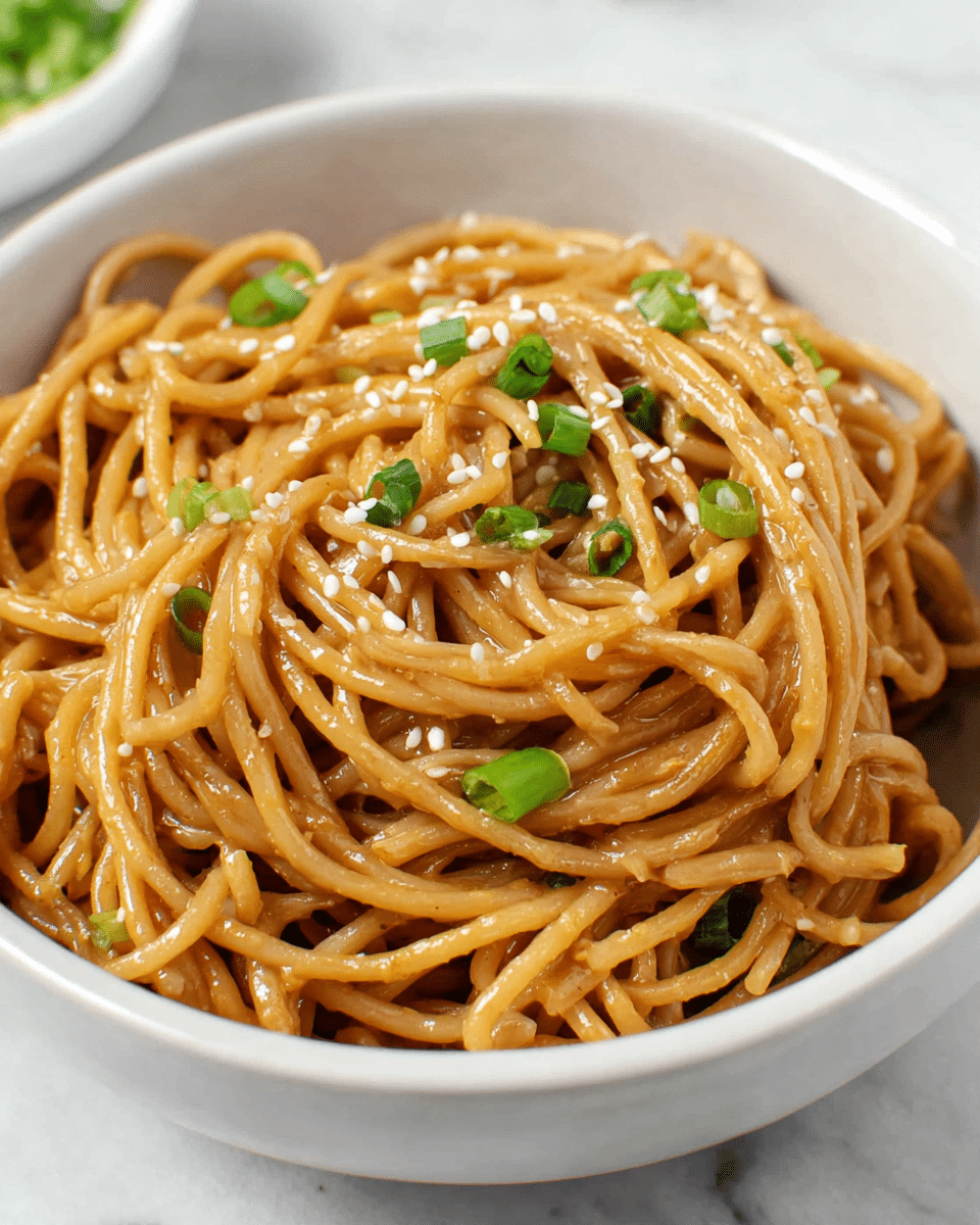 A close-up view of a bowl filled with cooked spaghetti noodles coated in a light brown sauce. The noodles are twisted and piled loosely in about three layers, with a glossy texture showing they are well mixed with the sauce. On top and sprinkled throughout are small green slices of chopped green onions and small white sesame seeds adding contrast. The noodles and toppings sit in a simple white bowl placed on a white marbled surface. Photo taken with an iphone --ar 4:5 --v 7