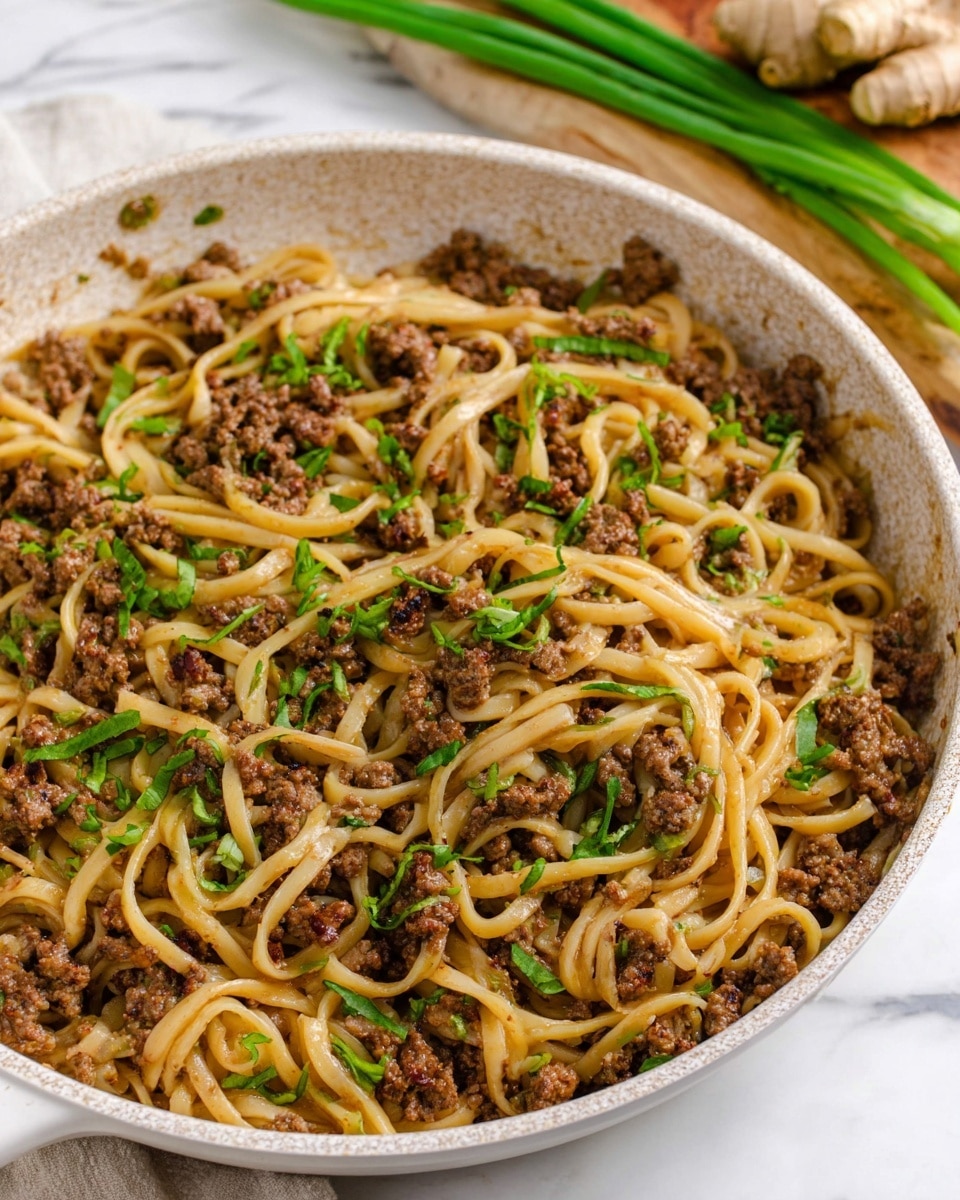 A round white speckled pan filled with one main layer of cooked noodles mixed with crumbled browned ground meat, scattered with small pieces of green chopped herbs on top for garnish. The noodles are light tan, long, and twisted around bits of meat that are dark brown and uneven in size. The pan rests on a white marbled surface, with blurred decor including green scallions and ginger in the background. Photo taken with an iphone --ar 4:5 --v 7