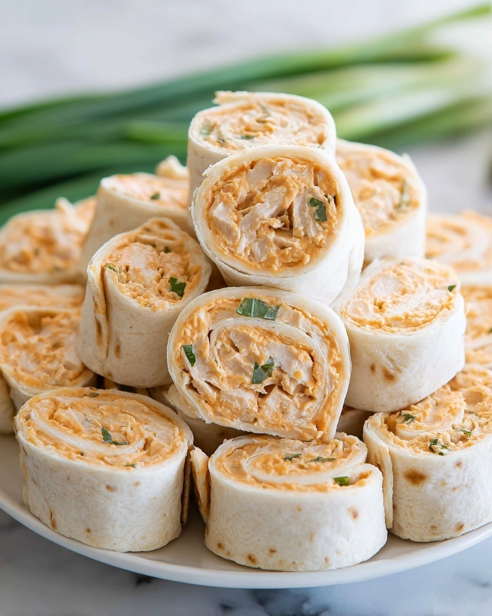 A close-up view of a white plate stacked with many tortilla pinwheel rolls, each cut into thick slices. Each roll has two layers: the outer layer is a pale white soft tortilla, and the inner filling is a creamy orange spread mixed with bits of light beige chicken and small pieces of green herbs. The pinwheels are neatly arranged in a slightly uneven pile on a white marbled surface, and some unopened green onions are blurred in the background. Photo taken with an iphone --ar 4:5 --v 7