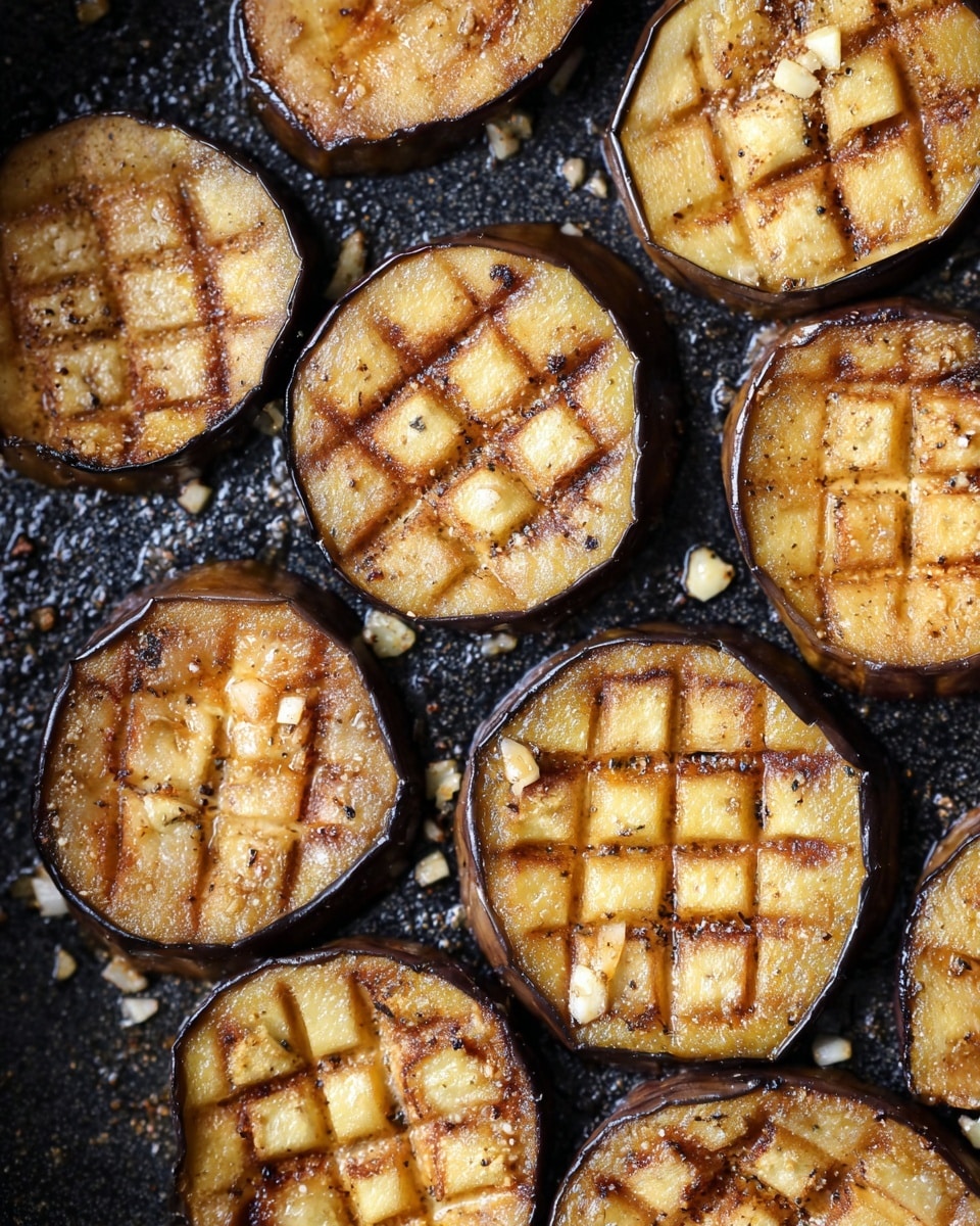 The image shows several round slices of eggplant arranged closely together in a black frying pan. Each slice has a crisscross pattern cut into the top surface, creating small square sections. The eggplant is cooked to varying shades of golden brown with some edges darker and caramelized. Small bits of what looks like minced garlic and pepper are scattered around the slices on the pan. The textured surface of the pan contrasts with the smooth, slightly shiny surface of the cooked eggplants. photo taken with an iphone --ar 4:5 --v 7