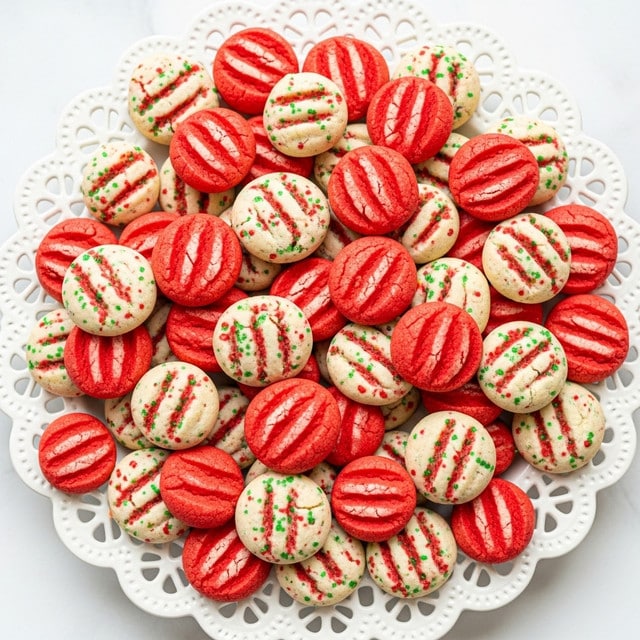 A white, round plate with a lace-like edge full of small, round cookies in three colors: bright red, green, and white with red and green sprinkles. Each cookie has three deep fork-pressed lines across the center, giving a striped texture. The cookies are piled high and mixed evenly, showing a smooth and slightly cracked surface. The background is soft with a white marbled texture, giving a fresh and clean look. photo taken with an iphone --ar 4:5 --v 7