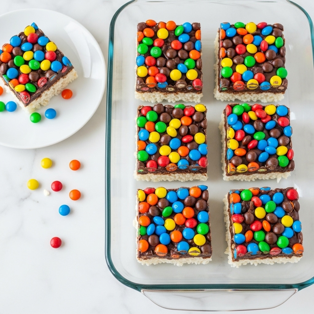 The image shows a clear glass baking dish with six square treats arranged in two rows. Each treat has three layers: a bottom white, crispy rice base, a middle layer of sticky chocolate, and a thick top layer of colorful candy-coated chocolate pieces in red, yellow, blue, green, orange, and brown covering the entire surface. Some candies are also scattered around the dish. To the left, a white plate holds one treat, with a few candies spread on the white marbled surface around it. The scene is bright and colorful, with a clean white marbled background. photo taken with an iphone --ar 4:5 --v 7