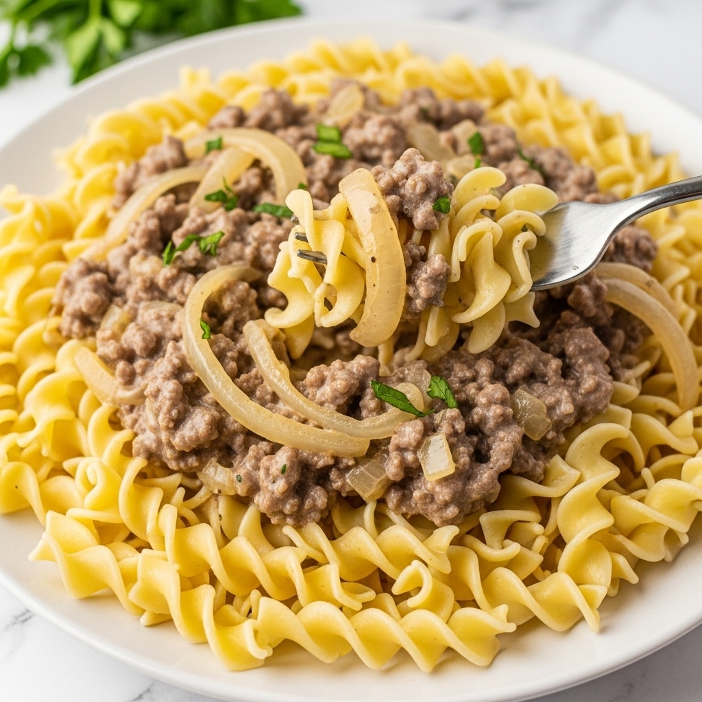The image shows a white plate with wavy egg noodles forming the base layer, light yellow in color and soft in texture, covering the whole plate. On top is a creamy sauce mixed with browned ground meat and translucent cooked onions, spread evenly over the noodles. A fork is lifting a bite of noodles and sauce, showing the sauce's thick and creamy texture clinging to the noodles. Small bits of green herbs are scattered on the sauce for garnish. The background is a white marbled surface with some green herbs out of focus behind the plate. photo taken with an iphone --ar 4:5 --v 7
