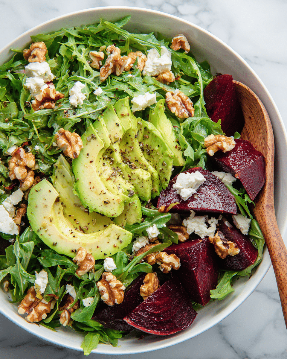 A white bowl filled with a fresh salad showing three main layers: a base of bright green arugula leaves with soft, jagged edges, topped with slices of creamy green avocado sprinkled with black pepper, and deep purple beet wedges that add rich color. Scattered on top are chunks of light brown walnuts and small white pieces of crumbled cheese, all glistening slightly as if lightly dressed. A wooden spoon rests on the right side of the bowl, partially buried under the salad. The bowl sits on a white marbled surface. photo taken with an iphone --ar 4:5 --v 7
