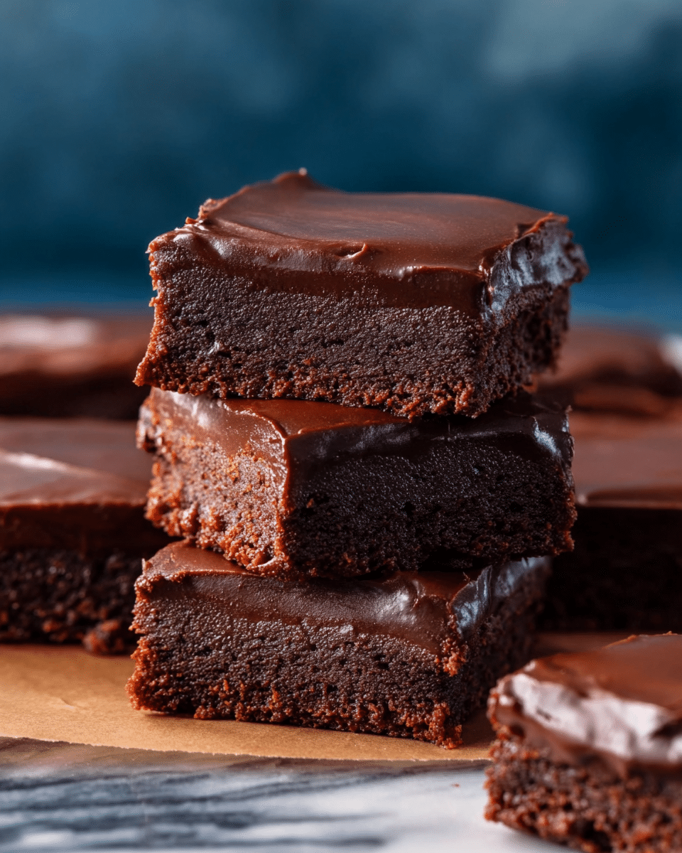 The image shows a stack of three chocolate squares, each square having two layers: a dense, crumbly dark brown brownie base and a thick, glossy chocolate ganache top. The ganache layer is smooth and shiny, slightly thicker than the brownie base, creating a rich and moist contrast. Surrounding the stack are more cut squares laid flat, showing the consistent two-layer structure across all pieces. The scene is set on a white marbled surface with a blurred dark blue background, enhancing the deep chocolate colors. photo taken with an iphone --ar 4:5 --v 7