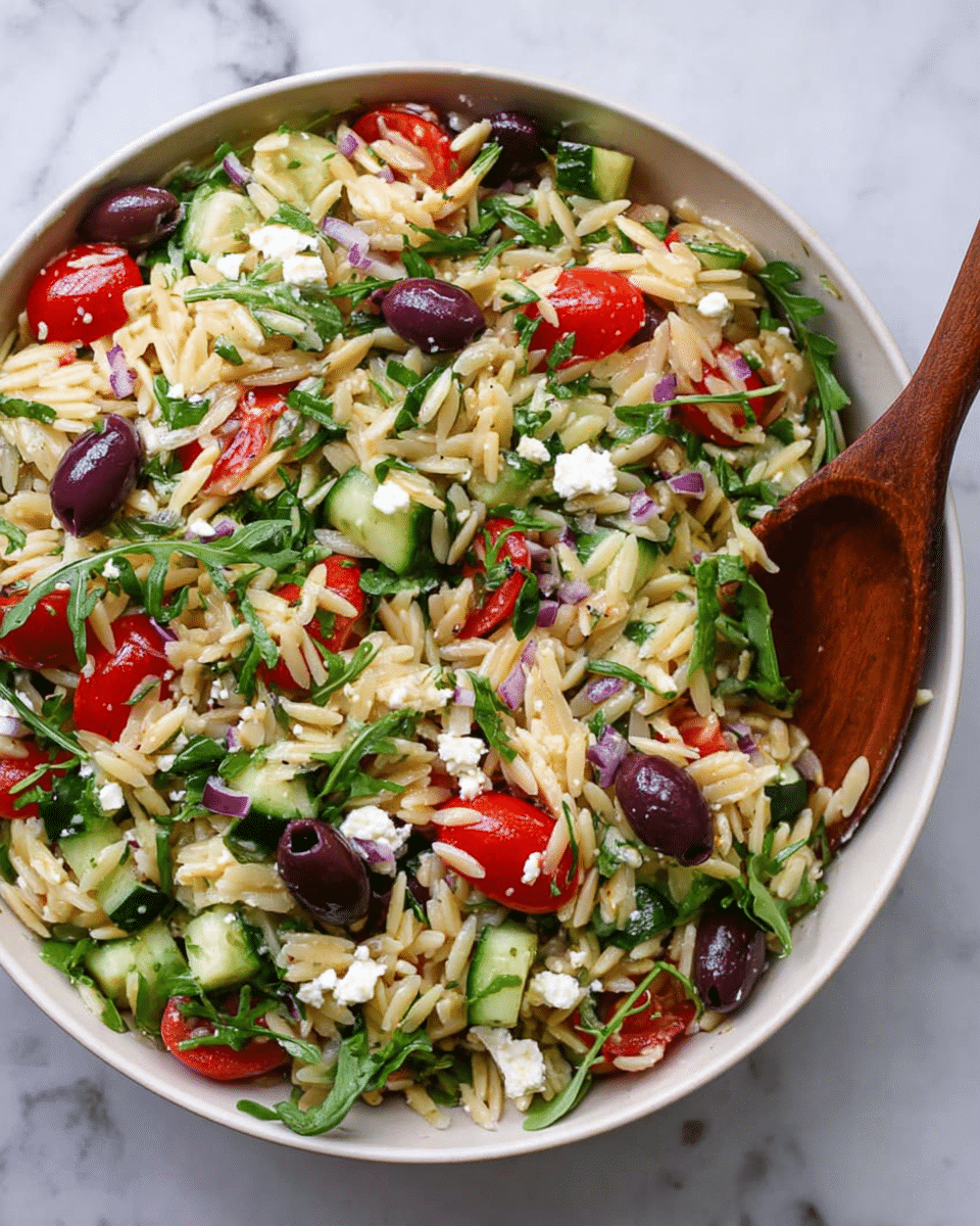 A white bowl filled with a colorful orzo pasta salad showing multiple layers: the base layer is light golden orzo pasta mixed with dark purple sliced olives, bright red halved cherry tomatoes, and chunks of green cucumber. Scattered throughout are small pieces of white feta cheese and fresh dark green arugula leaves with hints of chopped red onion adding tiny purple bits. A wooden spoon is partially dipped into the salad on the right side. The dish is placed on a white marbled surface. photo taken with an iphone --ar 4:5 --v 7