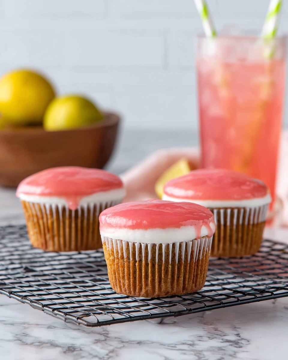 Three cupcakes sit on a black wire cooling rack over a white marbled surface. Each cupcake has three visible layers: the bottom baked cake layer is light brown, the middle layer is white frosting, and the top layer is a smooth, glossy pink glaze. In the background, there is a blurred wooden bowl holding yellow fruits on the left and a clear glass filled with pink iced drink with a green and white striped straw on the right. photo taken with an iphone --ar 4:5 --v 7