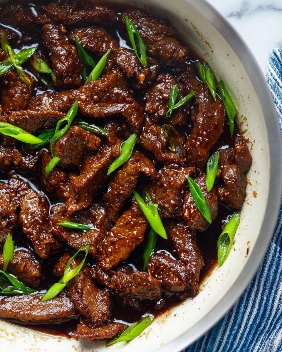 The image shows a close-up of cooked beef strips in a white skillet. The beef slices are dark brown, shiny, and coated with a rich, glossy sauce that gives them a slightly oily texture. Bright green chopped scallions are scattered evenly over the beef, adding fresh color contrast. The skillet rests on a white marbled surface with a blue and white striped cloth nearby. The beef pieces vary slightly in shape and size, and the sauce pools lightly around them. Photo taken with an iphone --ar 4:5 --v 7