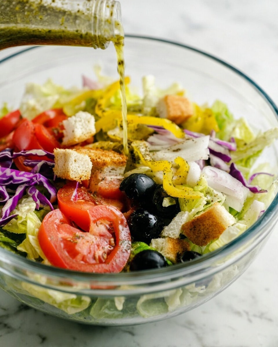A clear bowl filled with a fresh salad showing several layers: the base layer is light green chopped lettuce with a crisp texture, mixed with shredded purple cabbage; scattered on top are bright red tomato slices with visible seeds, whole black olives, yellow pepperoncini peppers, thin slices of white onion, and small cubed pieces of light brown croutons. A woman's hand is pouring a green herb dressing from a bottle above, creating a stream over the salad. The bowl sits on a white marbled surface. Photo taken with an iphone --ar 4:5 --v 7