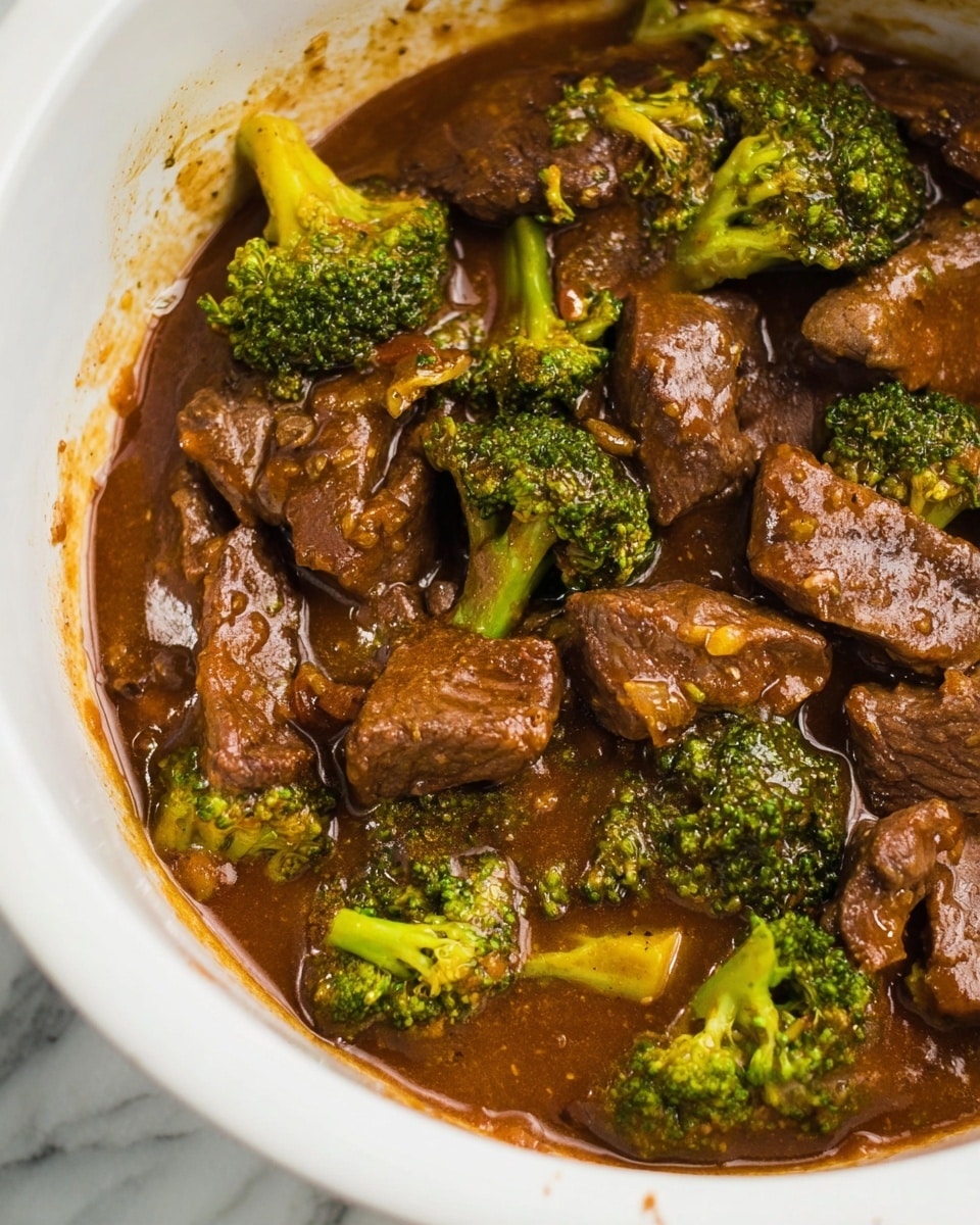 The image shows a close-up of a white bowl filled with beef and broccoli in a thick, brown sauce. The dish has large chunks of brown beef mixed with bright green broccoli florets that are coated in the glossy sauce. The sauce has a rich texture with some small bits visible, clinging to the meat and vegetables, and some sauce stains can be seen on the sides of the bowl. The background is a white marbled surface. photo taken with an iphone --ar 4:5 --v 7