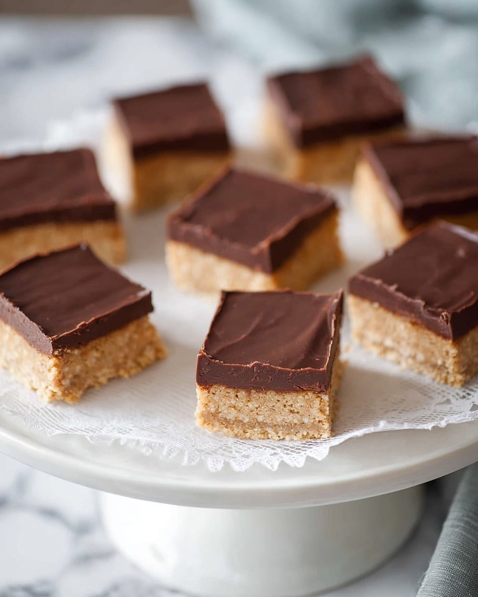 Nine square dessert bars are arranged on a white cake stand with a lace edge, set against a background of white marbled texture. Each bar has two layers: the bottom layer is thick and light brown with a textured, slightly crumbly look, while the top layer is a smooth, glossy dark brown chocolate coating that evenly covers the bars. The bars are placed close to each other, some showing clean edges, and others with slightly uneven chocolate tops. Photo taken with an iphone --ar 4:5 --v 7