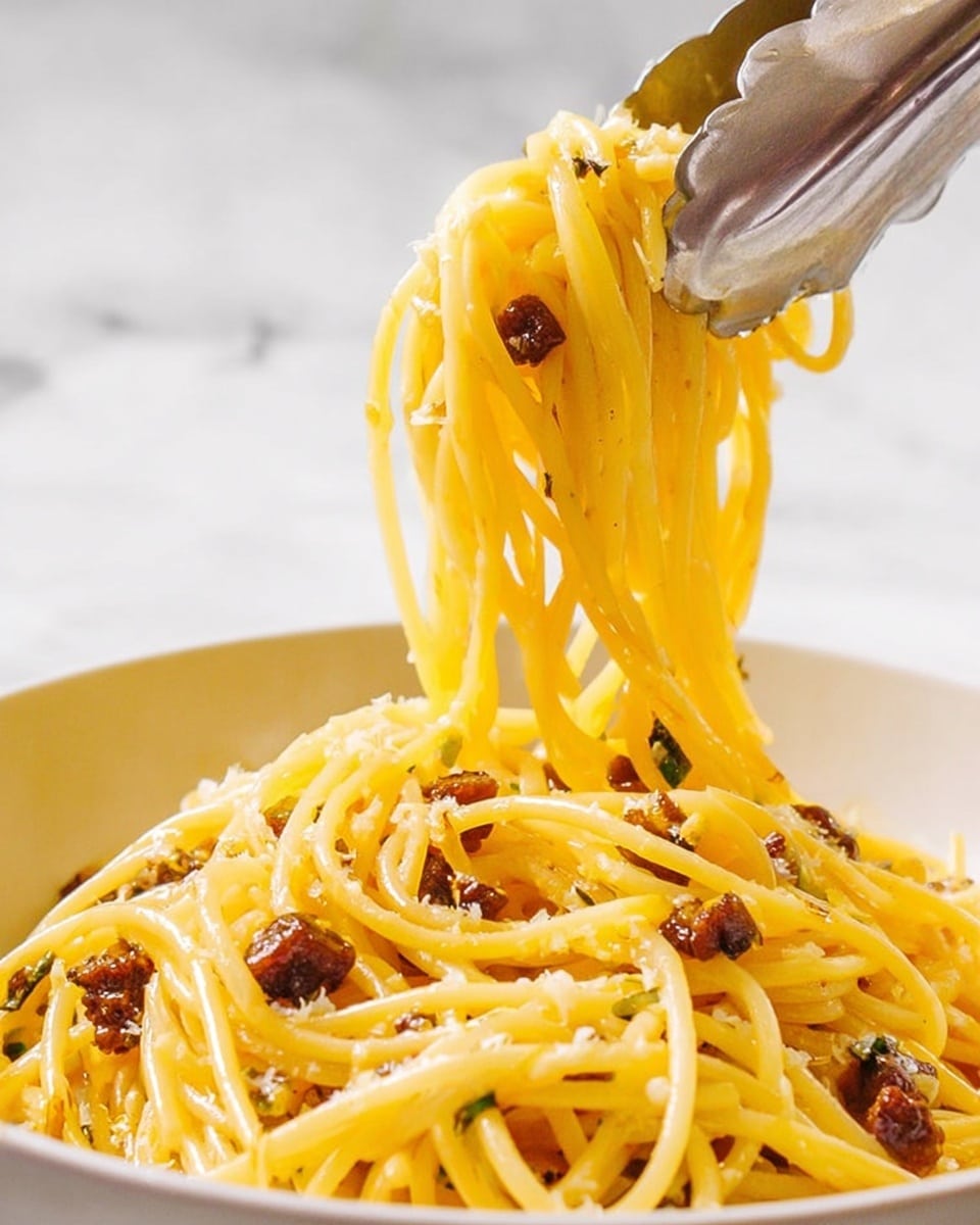 A close-up of a white bowl filled with shiny, yellow spaghetti noodles that are coated in oil or sauce, mixed with small, dark brown cubes of cooked meat scattered throughout. A pair of silver tongs lifts a portion of the noodles above the bowl, showing the noodles in mid-air, tangled and glistening. The background is a white marbled texture. photo taken with an iphone --ar 4:5 --v 7